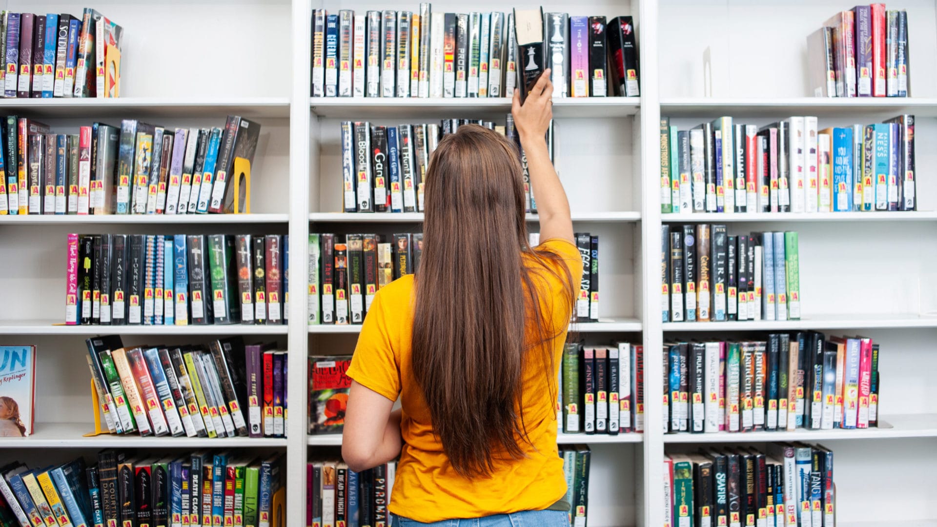 woman with long hair puts a book on the shelf