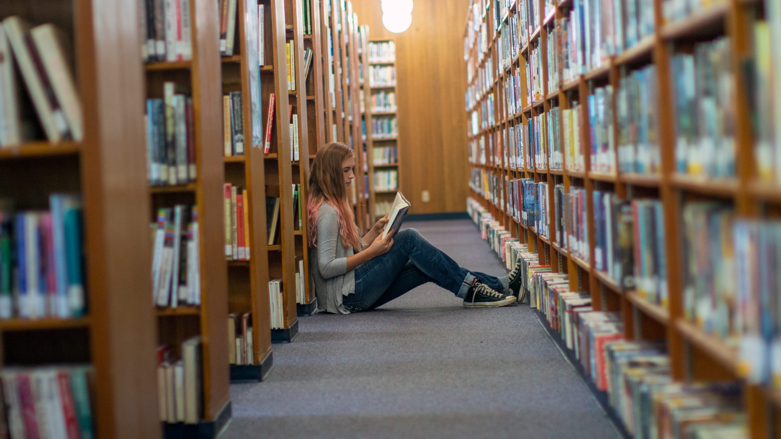 teen girl sitting on the floor in row of library shelves