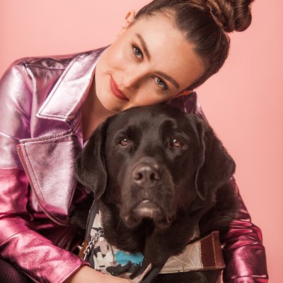women in pink shiny jacket hugging a black dog resting her head on the dogs head