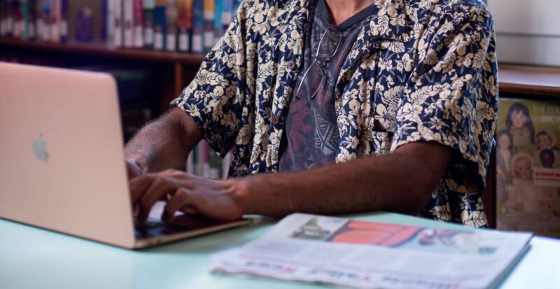 man with hawaiian shirt on a laptop with newspaper by him