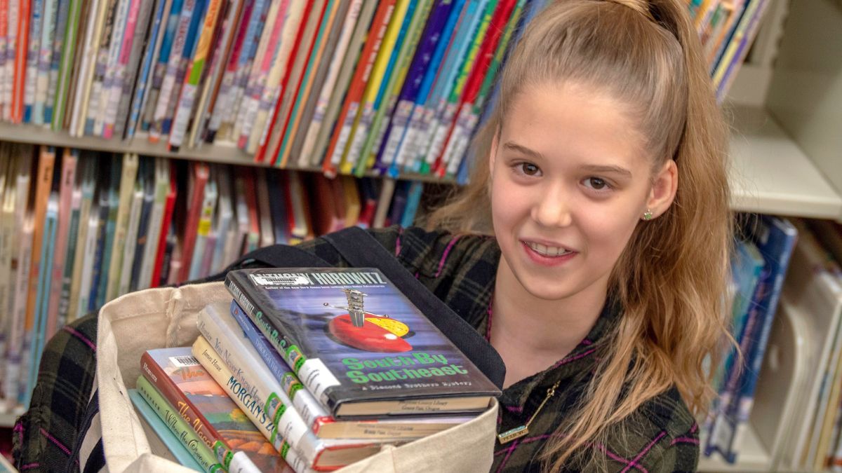 Young girl with blonde hair hold bag filled to the top with books