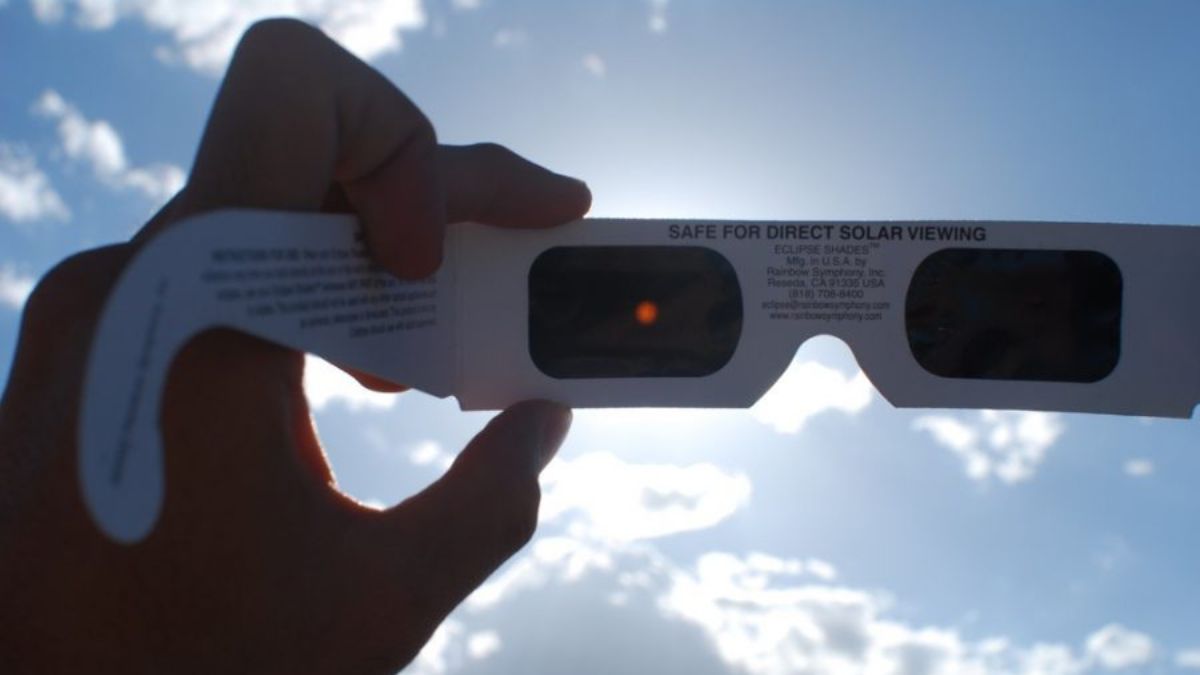 closeup of hand holding solar eclipse glasses in the sky to view an eclipse