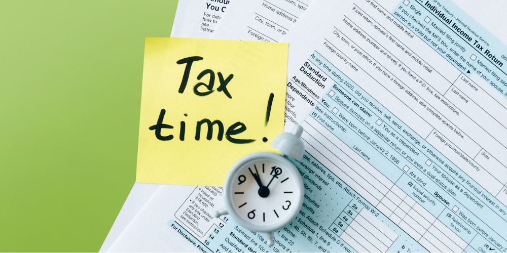 tax forms layflat with a white clock and a yellow sticky note that says "Tax Time!" on top