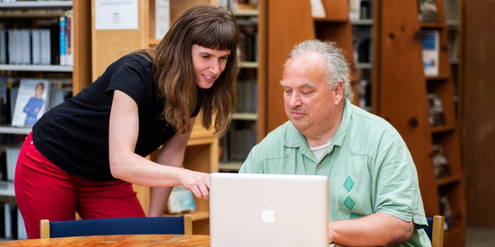 woman points at silver laptop computer while man in green shirt types