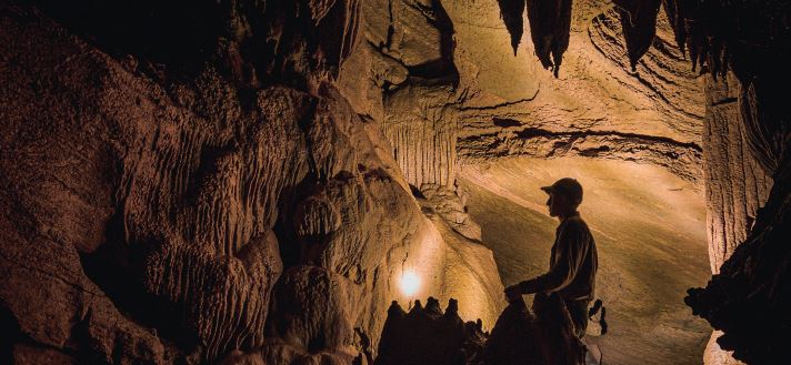 A man standing in a dark cave shining a flashlight at the cave wall.