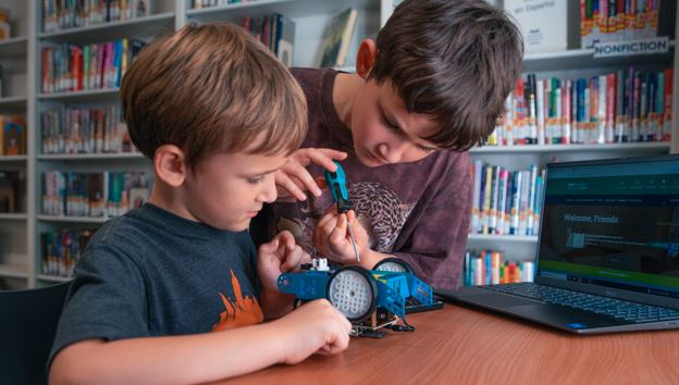 Two young boys building a STEM robot kit with a laptop open infront of them in the teen room of the Grants Pass library.